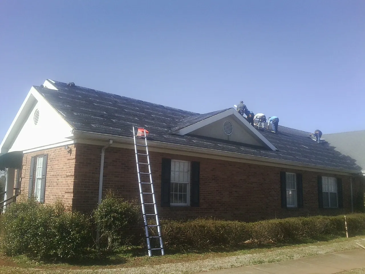 Crew tearing shingles off a brick ranch roof with a ladder set — Metal Roof Repair work by our crew in Fairview